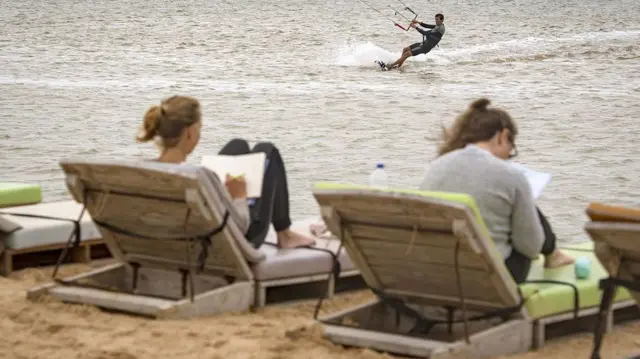 deux vacanciers européens profitent du soleil sur des transats au bord de l'océan à dakhla, tandis qu'un troisième s'adonne au kitesurf